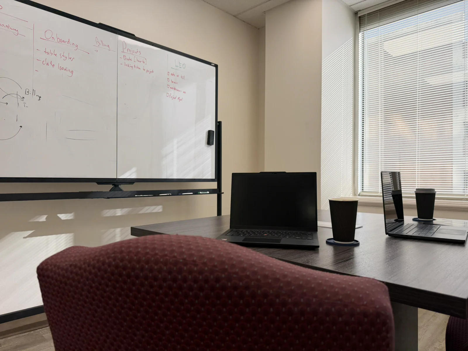 A huddle room: a rolling whiteboard of planning notes beside a small table with laptops and coffee.